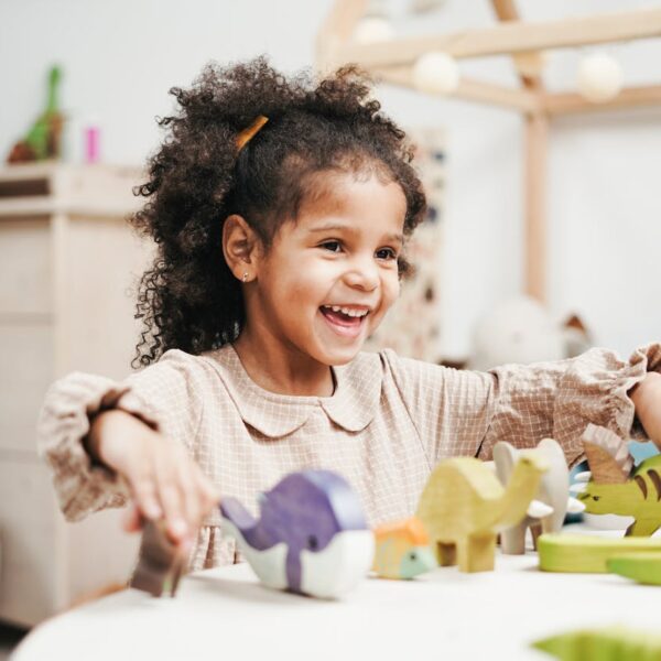 Selective Focus Photo of Laughing Young Girl Playing with Wooden Toys on White Table